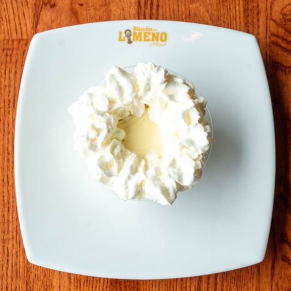 Peruvian dessert with whipped cream and a creamy yellow center on a white plate with the Rincon Limeno logo.