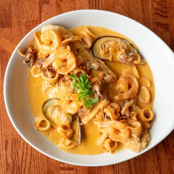Peruvian seafood dish with shrimp, mussels, and calamari in a creamy orange sauce, garnished with parsley.