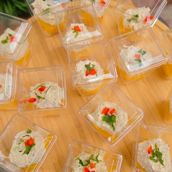 Numerous small clear plastic containers with white dip, orange sauce, and red pepper garnish.