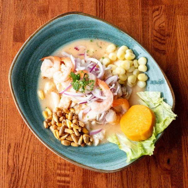 Peruvian ceviche with shrimp, white fish, red onion, corn, sweet potato, and lettuce on a blue plate.