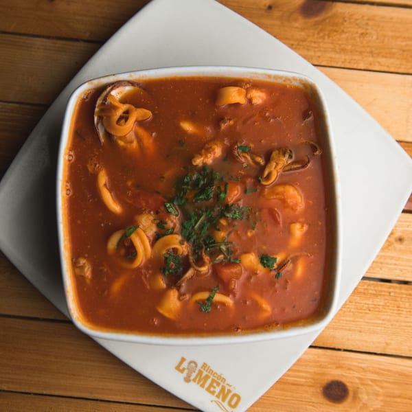 Peruvian seafood soup with squid, shrimp, and mussels in a rich red broth, garnished with parsley.