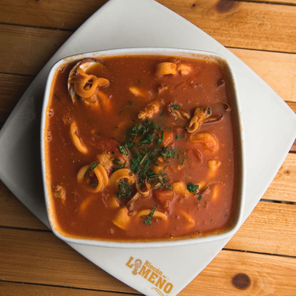 Peruvian seafood soup with squid, shrimp, and mussels in a rich red broth, garnished with parsley.