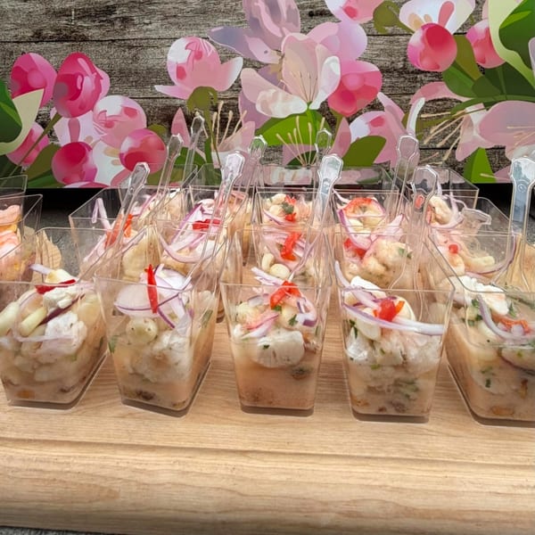 Rows of ceviche appetizers in small clear cups with spoons, garnished with red onion and peppers.