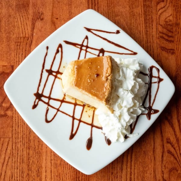 A slice of Peruvian flan with caramel sauce and whipped cream on a white plate.
