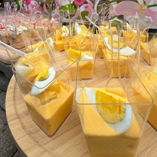 Rows of small square cups filled with yellow sauce, topped with hard-boiled egg and potato.