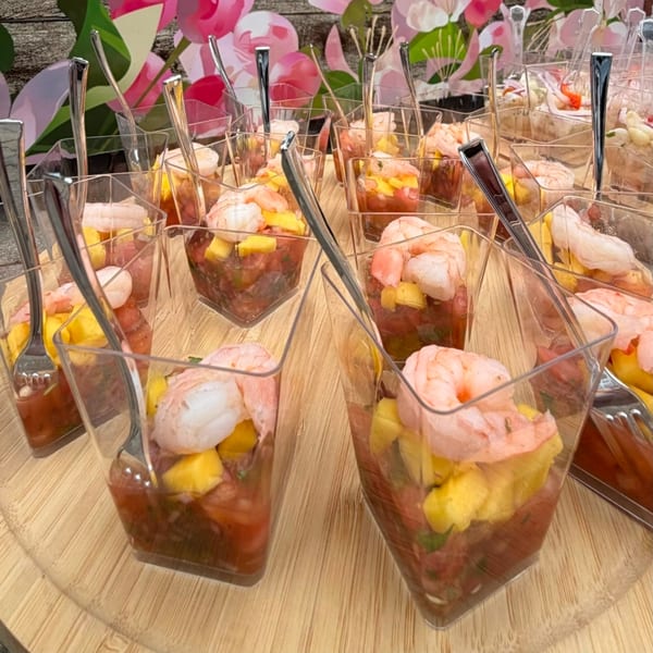 Many small clear cups filled with shrimp, mango, and salsa, each with a tiny fork.